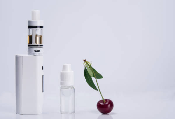 vapor device, e-liquid bottle and cherry sitting on white surface with white background