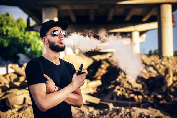 Man with beard vaping outdoors in sunglasses